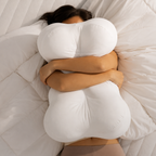 Person hugging a large white pillow on a bed