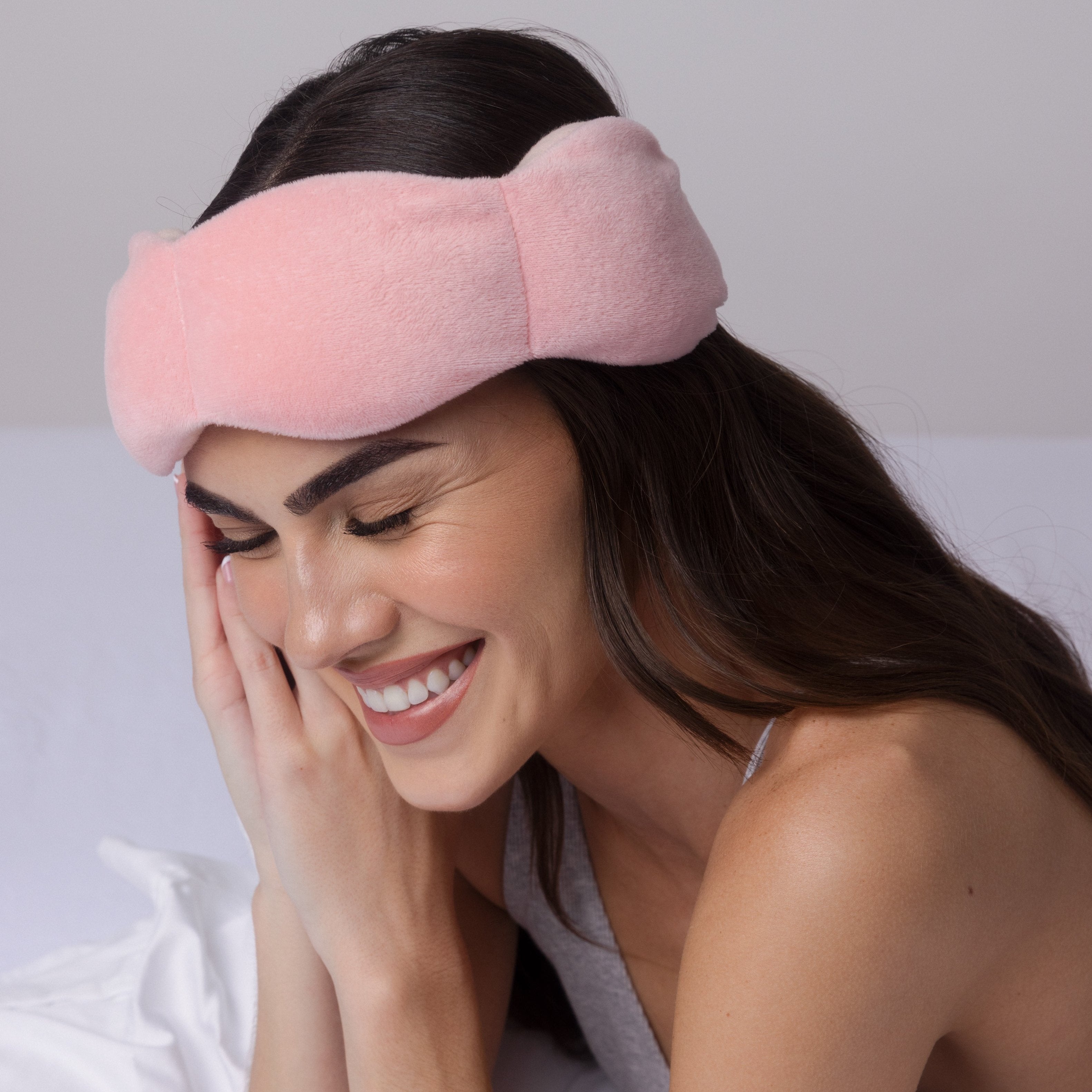 Woman wearing a pink eye mask on a neutral background