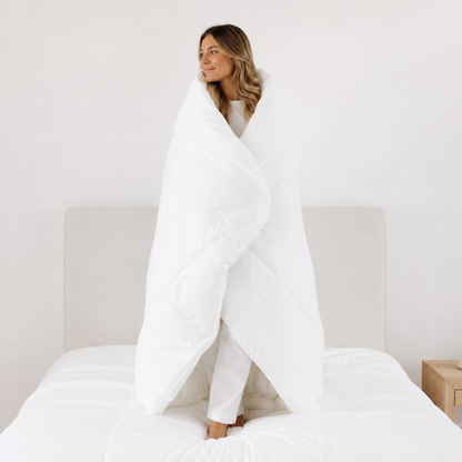 Woman wrapped in a white blanket on a bed in a minimalistic room.