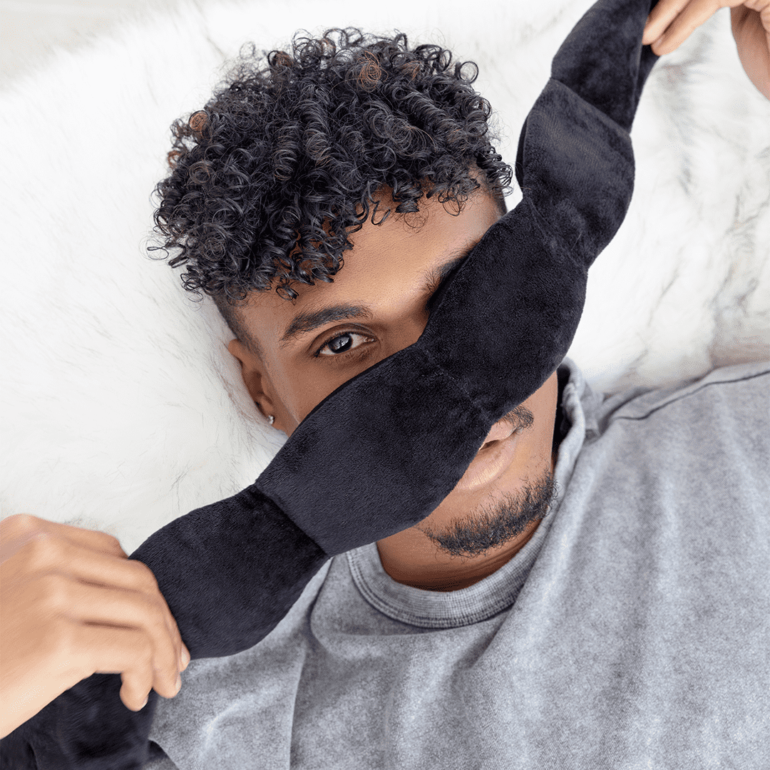 Person wearing a black sleep mask in bed