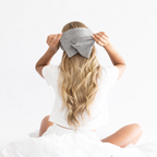 Person wearing a gray sleep mask with a plain white background